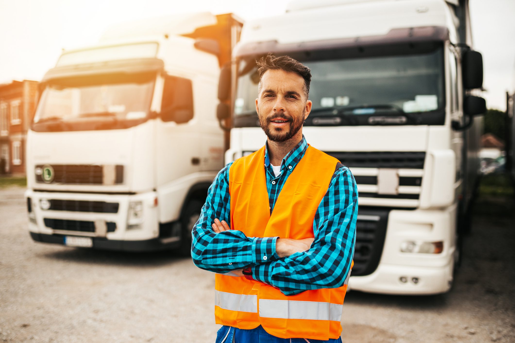Man in safety vest standing by trucks.