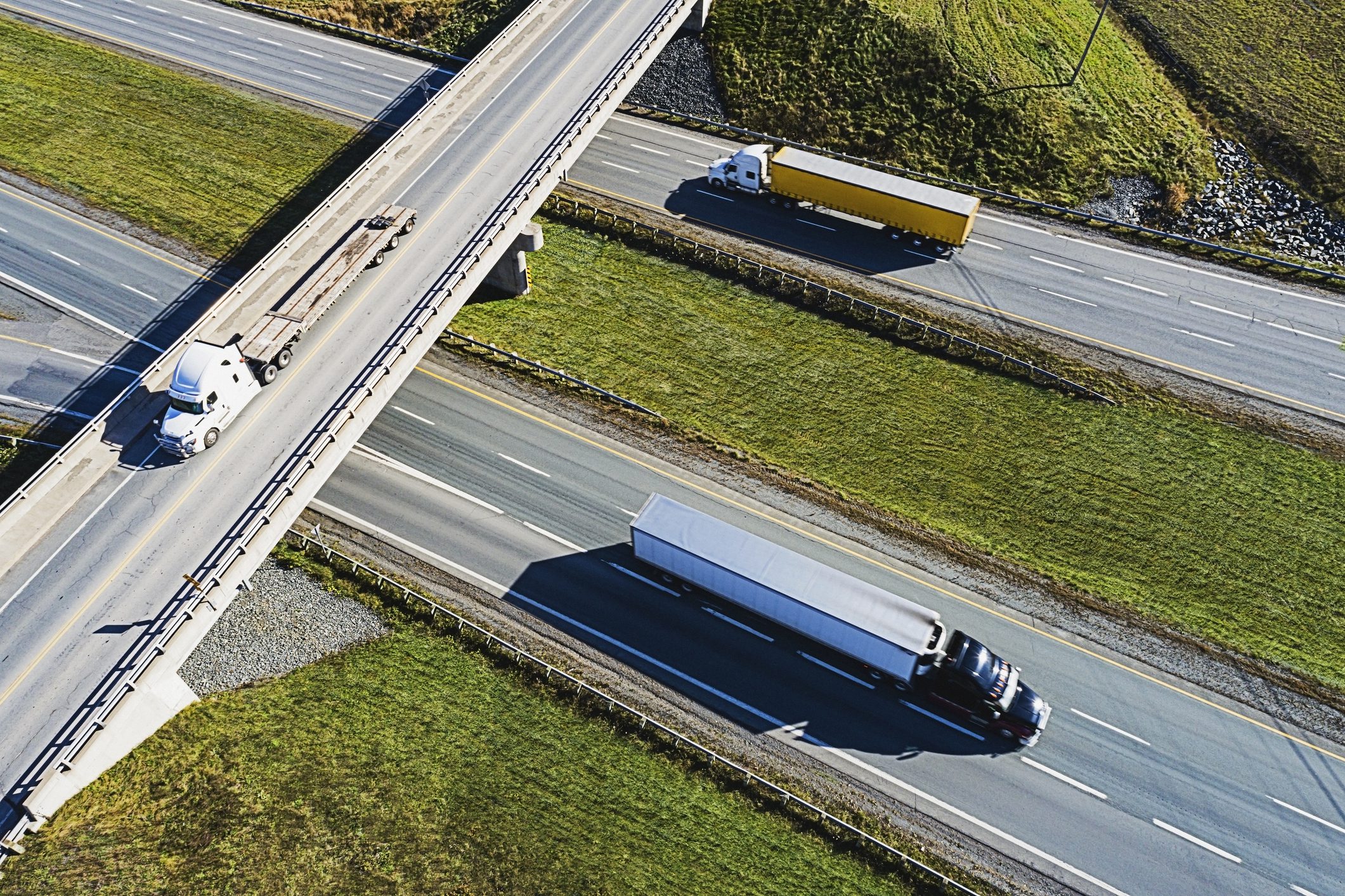 Trucks on highway with overpass, aerial view.