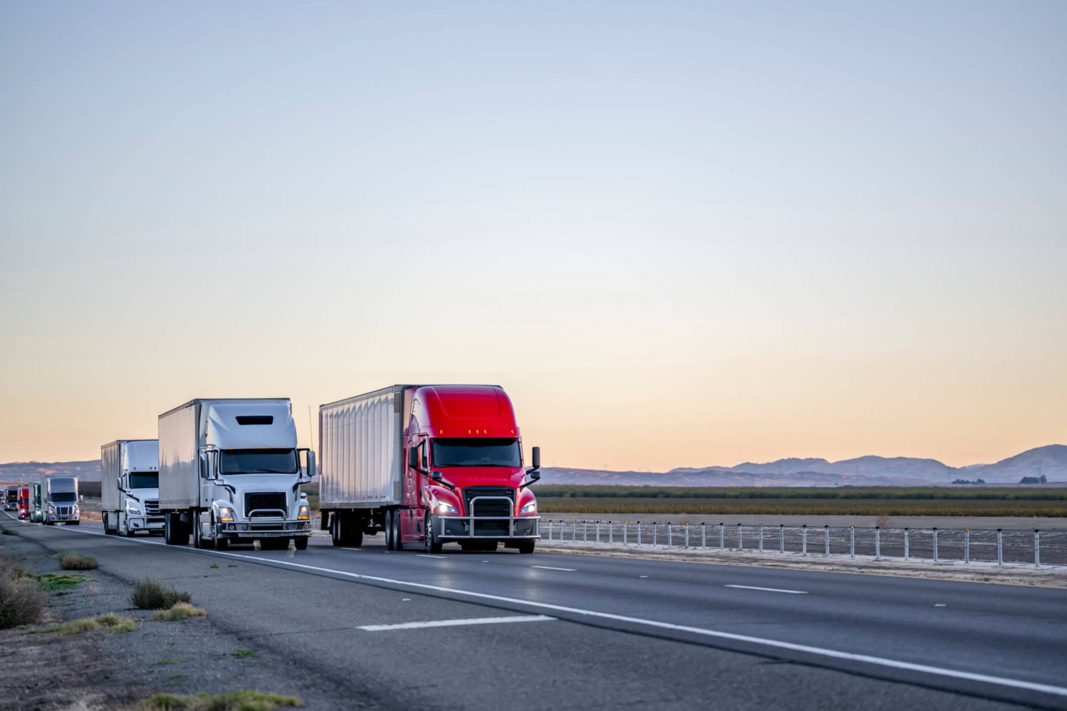 Trucks driving on highway during sunset.